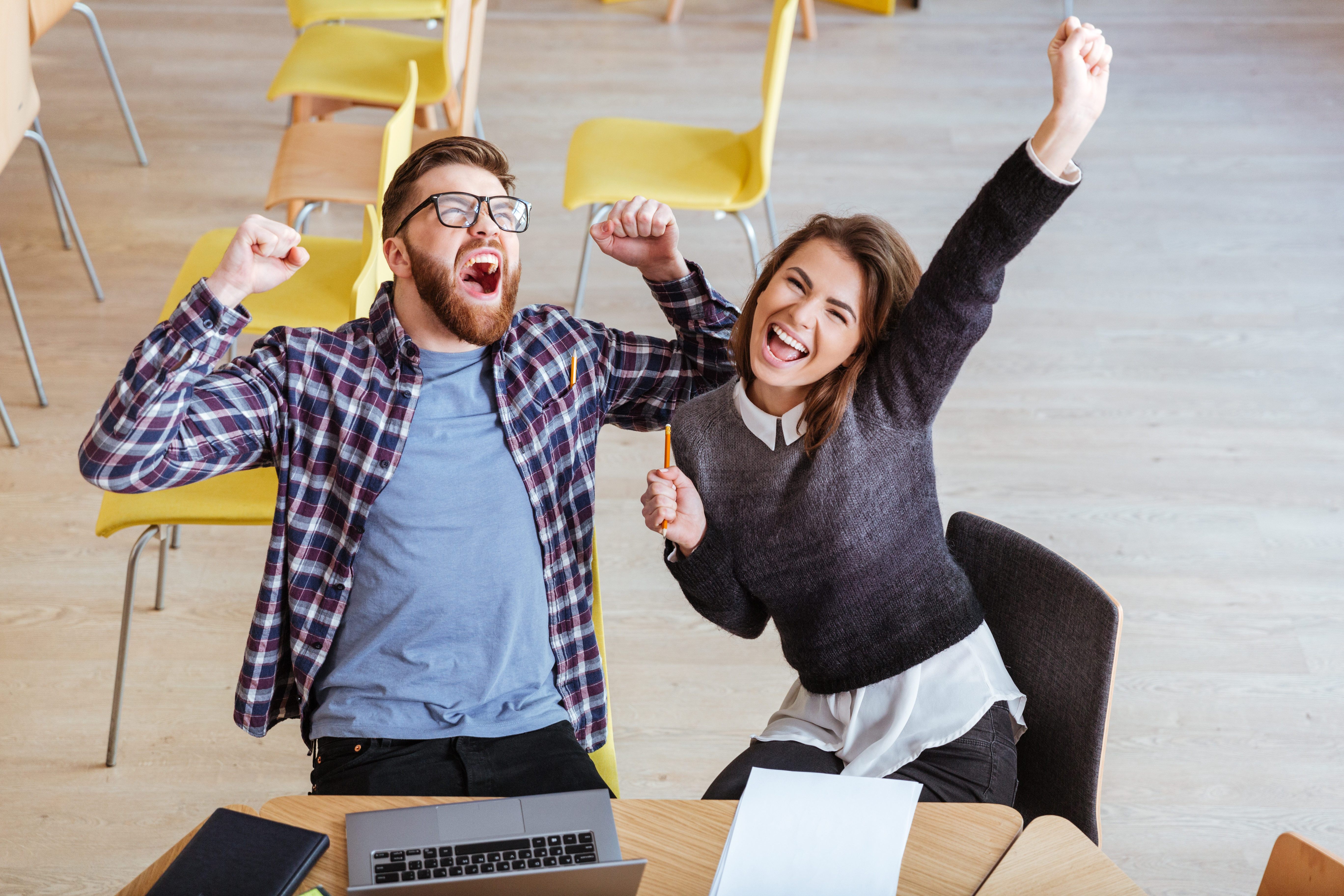 Happy students sitting in library make a winner gesture.