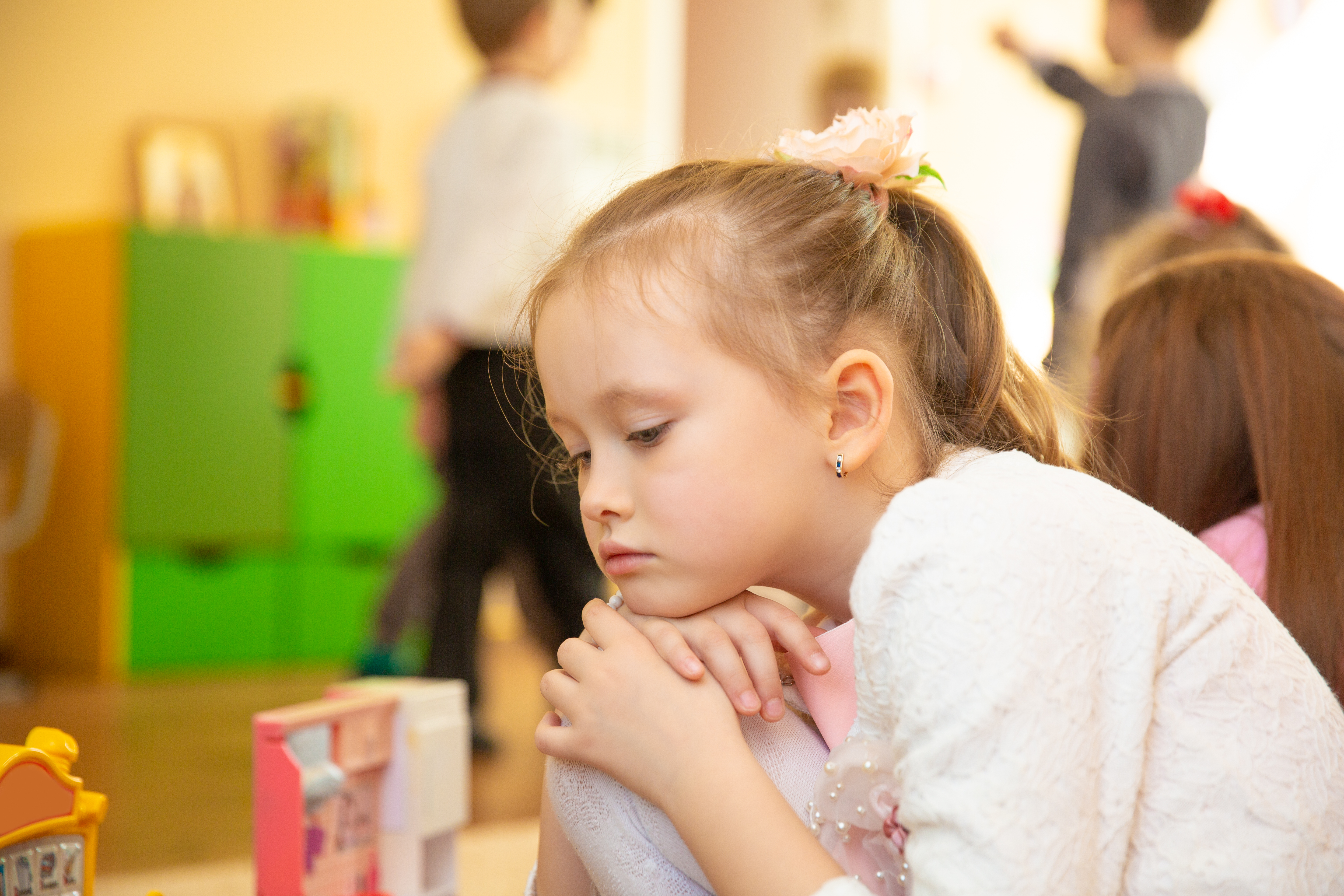Portrait of sad blond little girl sitting in kindergarten